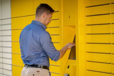 Çağdaş bir ortamda, bir adam paketini kolaylık için tasarlanmış parlak sarı bir dolaptan alır.