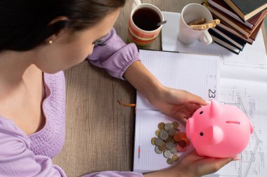 Bir kadın, banknotlar ve bir fincan sıcak kahveyle çevrili neşeli bir kumbarayla tüm birikimini incelikle analiz ediyor.