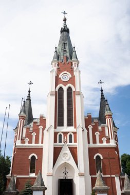 Göz kamaştırıcı Gotik tarzı bir kilise. Yüksek kuleleri ve parlak gökyüzünün altında belirgin bir saat kulesi var..