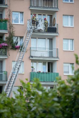 İtfaiyeciler bir apartmanın balkonunda merdiven kullanarak acil durum müdahalesi yapıyorlar..