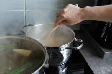 Bir el, sobanın üzerinde çeşitli malzemelerle dolu bir tencereyi karıştırır ve canlı pişirme sürecini harekete geçirir.