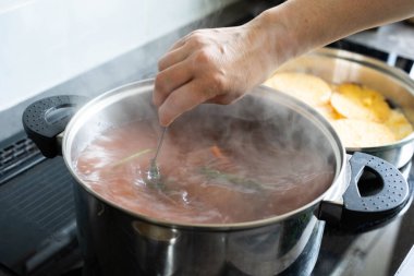 Bir el kaynayan bir çorba tenceresini karıştırıyor, ev yemeğinin özünü güzelce gösteriyor ve buhar yükseliyor.