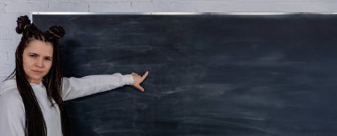 Moda saçı olan şık bir kadın kendine güvenerek boş bir tahtaya işaret ediyor. Bir şeyler öğretmeye ya da açıklamaya hazır.