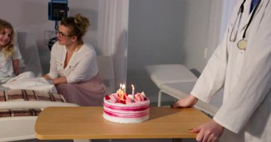 Bir çocuk, anne ve doktorun doğum gününü hastanede pastayla kutladıkları neşeli bir an.