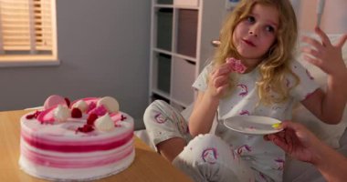 Küçük bir kız, bir hastane yatağında oturmuş, tatlı bir anı yaratırken pasta diliminde neşe buluyor.