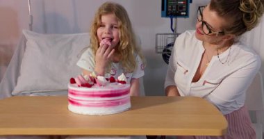 Yürek ısıtan bir kutlama başlıyor. Bir kız ve bir kadın, hastane ortamında lezzetli bir pastayı neşeyle paylaşıyorlar.