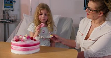 Genç bir kız ve bakıcısı, hastane ortamında bir pasta eşliğinde kalpten bir kutlama yapıyorlar.