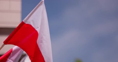 Canlı ve renkli bir Polonya bayrağı açık mavi gökyüzünün altında canlı bir halk toplantısında gururla sergileniyor.