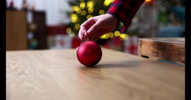 Bir el, ışıl ışıl, parlak kırmızı bir süsü hoş bir tatil ortamının ortasında güzel, ışıl ışıl parlayan bir ağaçla nazikçe kaldırır.