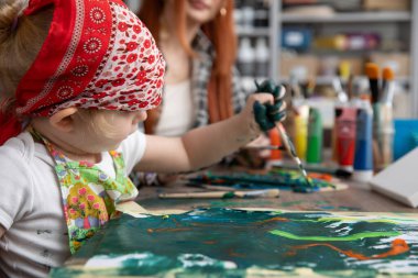 Canlı bir sanat stüdyosunda, neşeli bir sahne, mutlu bir anne figürünün yanında mutlu bir şekilde resim yapan bir çocukla gözler önüne seriliyor.