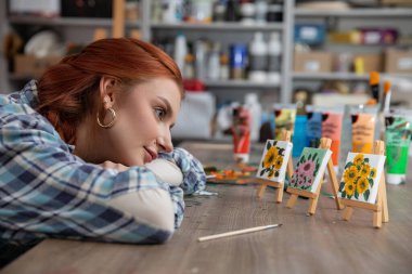 Genç bir sanatçı yaratıcı malzeme ve aletlerle dolu bir stüdyodaki canlı resim koleksiyonuna hayran.