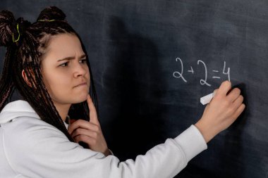 Bir öğrenci, karatahta üzerinde karmaşık bir matematik denklemi çözmek için özenle çalışırken derin düşüncelere dalmıştır.