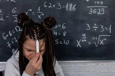 Bir öğrenci tahtaya yazılmış matematik denklemlerine meydan okuyarak çalışırken gözle görülür şekilde hayal kırıklığına uğramış görünüyor.