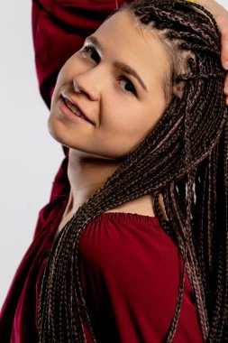 Neşeli ve hayat dolu genç bir kadın gururla örülmüş karmaşık saç stilini, kendine güvenini ve tarzını sergiliyor.