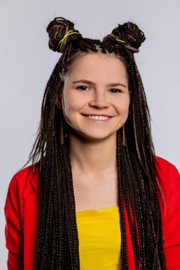 Neşeli genç bir kadın, parlak ve canlı bir kıyafet giyerken eşsiz örgülü saç stilini gururla sergiliyor.