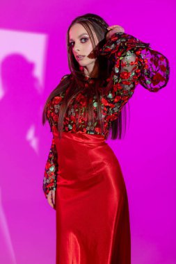 Göz kamaştırıcı bir portre, göz kamaştırıcı kırmızı bir elbise içinde, güzel pembe bir arka planda.