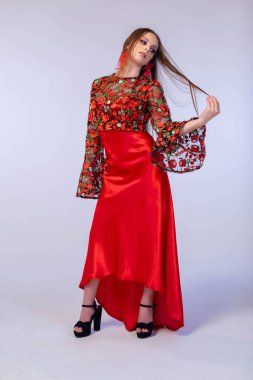 Şık manken, çiçekli kolları ve yüksek topuklu ayakkabıları olan zarif kırmızı bir elbise sergiliyor.