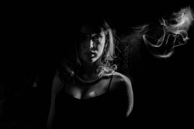 Gizemli, gölgeli bir ortamda incilerle süslenmiş bir şahsın büyüleyici siyah beyaz portresi.