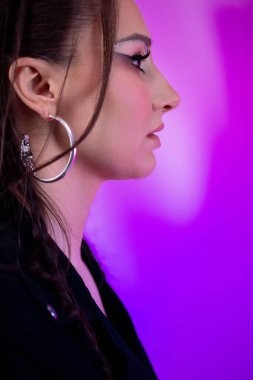 Büyüleyici bir yan profil, çağdaş makyaj setini canlı bir arkaplana karşı güzelce sergileyen bir kadın.