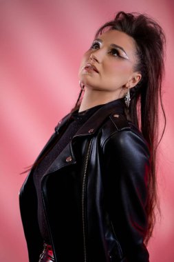 Göz kamaştırıcı bir manken, pembe arka planda deri ceket giyerken şık bir moda tarzını güzel bir şekilde sergiliyor.