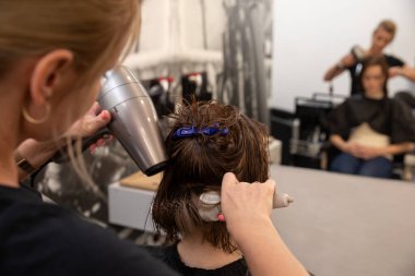 Yetenekli bir kuaför, şık ve modern bir kuaför ortamında müşterisine saç kurutma makinesi kullanıyor.