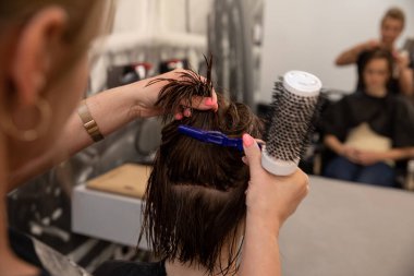 Yetenekli bir stilist, canlı ve canlı bir salon atmosferinde çeşitli aletleri olan bir müşterinin saçı üzerinde ustaca çalışıyor.