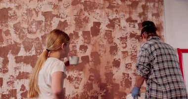 İki arkadaş yaratıcı boyama teknikleriyle sıkıcı bir duvarı canlandırıyor, takım çalışması ve ev dekorasyonu.