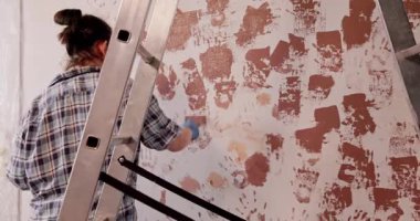 Bir insan, daha yüksek yerlere ulaşmak için ustalıkla bir merdivenin üzerinde dururken desenli bir duvarı sanatsal bir şekilde boyuyor.