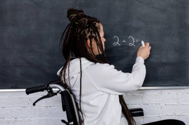 Tekerlekli sandalye kullanıcısı, tahtaya açık bir şekilde yazarak, bir çok kişiye ilham vererek kendine güvenen bir sınıf dersi verir.