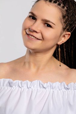 Kendine güvenen genç bir kadın modayı takip eden omuzlarının üstünde büyüleyici bir şekilde gülümseyerek örgülü saç stilini sergiliyor..