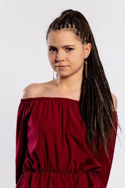 Kendine güvenen genç bir kadın omuz hizasında çarpıcı bir bordo elbise giyer ve güzel örgülü saç stilini sergiler.