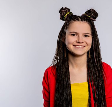 Neşeli, güler yüzlü bir kız eşsiz örgülü saç stili ve parlak moda elbisesiyle hava atıyor.