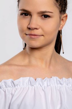 Yakın plan bir portre, omuzları açık şık beyaz bir bluz giyen, kendine güveni ve özgüveni olan genç bir kadını yakalar.