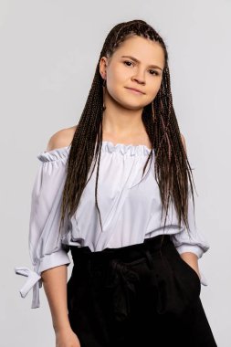 Genç bir kadın, şık bir omuz üstü giyinmiş ve şık bir siyah pantolon giymiş bir fotoğraf için özgüvenle poz veriyor.