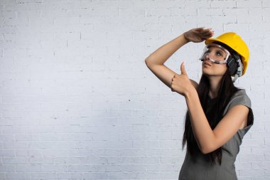 Sıkı bir şapka ve güvenlik teçhizatı takmış kendine güvenen genç bir kadın hareketli bir inşaat ortamının ortasında poz veriyor.