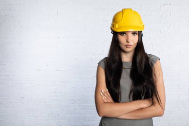 Kasketli kararlı bir kadın, güven içinde kollarını kavuşturarak poz verir. Yapıdaki gerçek gücü somutlaştırır.