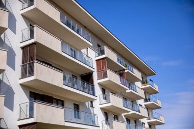 Açık mavi gökyüzünün arka planına karşı birden fazla balkon sergileyen çağdaş bir apartman kompleksi.