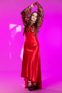Çarpıcı bir model, canlı bir arka planda eşsiz süsleri olan şık bir kırmızı elbise sergiliyor..