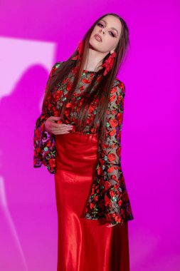 Çarpıcı bir model, canlı pembe bir arka planda çiçek desenli çarpıcı kırmızı bir elbise sergiliyor..