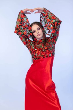 Zarif bir kadın kendine güveni tam kırmızı bir elbise içinde poz veriyor. Çiçek desenleriyle süslenmiş.