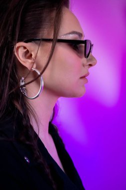 Canlı ve çarpıcı mor bir arkaplan karşısında zarif bir şekilde vurgulanmış modern gözlük taslayan şık bir profil çekimi.