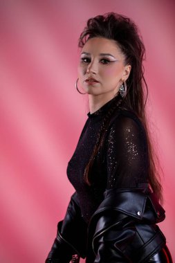 Şık ve şık bir kadın göz kamaştırıcı, parlak, siyah bir elbise içinde canlı pembe bir arka plana karşı poz verir.