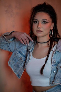 Genç bir kadın şık bir kot pantolon içinde şık aksesuarlarını ve canlı ifadesini sergiliyor.