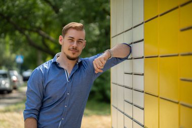 Mavi desenli gömlek giyen kendine güvenen genç bir adam şık bir şekilde parlak ve parlak sarı bir duvarın yanında poz veriyor.