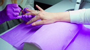 Yetenekli bir tırnak teknisyeni, profesyonel tırnak bakımı tekniklerini gösteren canlı bir kırmızı oje kullanır.