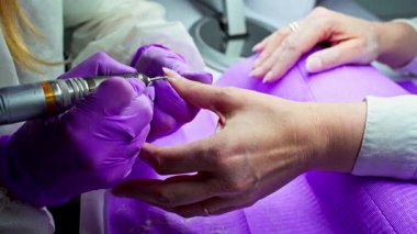 Uzman bir tırnak teknisyeni spa ortamında manikür hizmetleri için ustalıkla özel bir matkap kullanıyor.