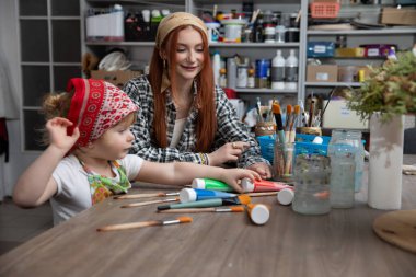 Canlı ve renkli bir sanat stüdyosunda, neşeli bir an, küçük bir çocukla bir ebeveyn arasında paylaşılır.