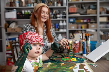 Bir çocuk renkli bir ev stüdyosunda deneyimli bir sanatçının yanında resim yaparken neşeli bir sanat seansı meydana gelir.