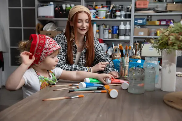 Canlı ve renkli bir sanat stüdyosunda, neşeli bir an, küçük bir çocukla bir ebeveyn arasında paylaşılır.