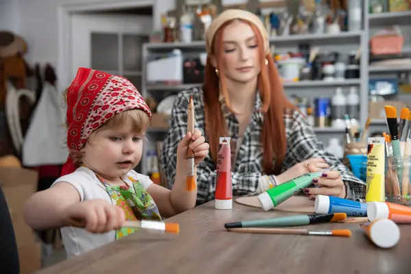 Bir çocuk, bir yetişkinle birlikte bir el sanatları masasında eğlenceli ve yaratıcı bir sanat seansının tadını çıkarıyor.